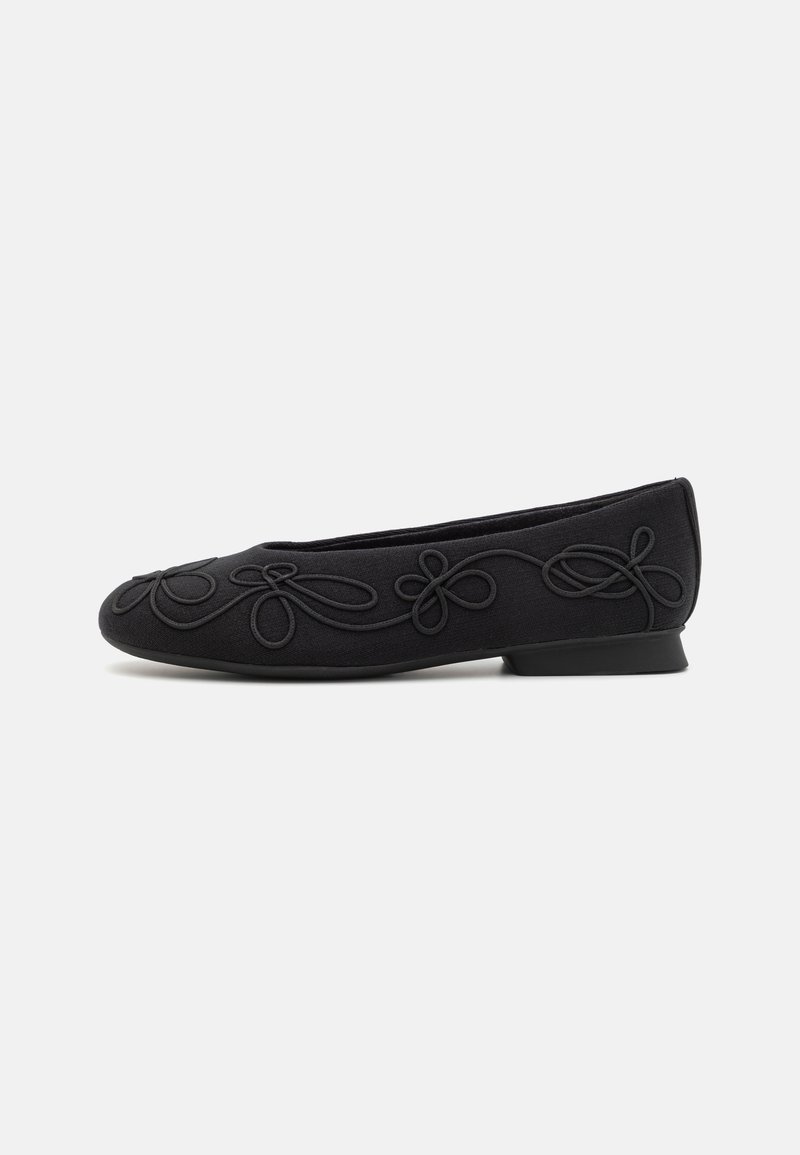 Chaussure de ballet noire plate avec un petit talon et des boucles brodées noires décoratives le long du côté, présentée de profil sur fond blanc.