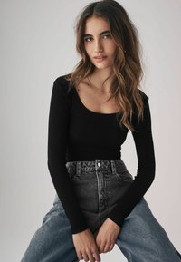 Sort langærmet ribbet top med rund halsudskæring, parret med højtaljede denim jeans i en falmet blå nuance, der har en frontknaplukning.