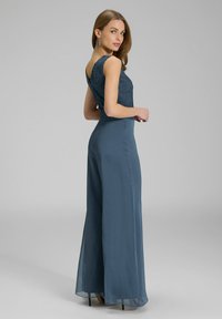 Jumpsuit long jusqu'au sol en bleu foncé, présentant un haut en dentelle et une coupe évasée. Texture lisse avec un dos en V. Agrémenté de détails subtils.