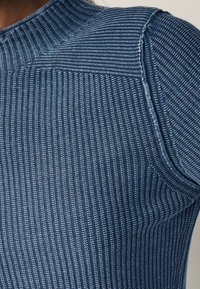 Prążkowana dzianina w ciemnoniebieskim kolorze z jaśniejszymi paskami, z wysoką szyją i skośnymi szwami na ramionach. Miękka tekstura i dopasowany krój.