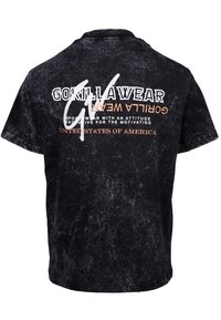 Korte zwarte T-shirt met een textuurafwerking. Voorzien van witte en oranje tekst op de achterkant: "GORILLAWEAR," "SPORTSWEAR MET HOUDE N" en "VERENIGDE STATEN VAN AMERIKA."