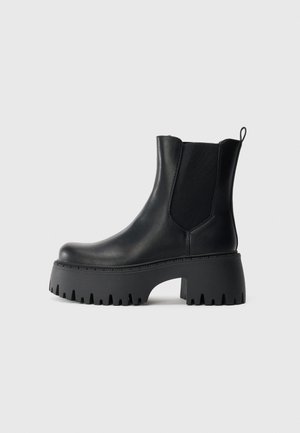 Bottine noire en cuir avec semelle épaisse à crampons, panneaux latéraux élastiques, tirette au talon et talon plateforme chunky surélevé.