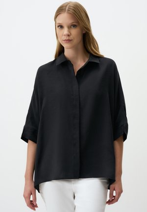 Black, loose-fitting shirt with a collar, button front, and short rolled sleeves. Smooth texture; longer back hem. Pair with white pants.