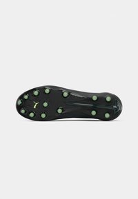 Semelle de crampons de soccer noire avec des crampons verts et un petit logo Puma vert sur un fond blanc uni.