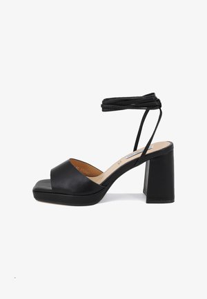 Sandalo con tacco nero e plateau, caratterizzato da una punta aperta e da un cinturino alla caviglia. Realizzato in pelle liscia con un tacco a blocco massiccio.