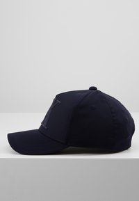 Cappellino blu navy con visiera curvata, dotato di un logo della lettera "Y" in rilievo sul davanti dello stesso colore. Realizzato in tessuto liscio.