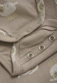 Beige baby romper met drukknoopjes en een wit schaapjespatroon bedrukt op de stof.