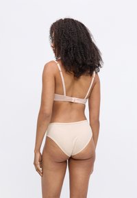 Nahtloser BH in Nude und passender hochgeschnittener Slip, ausgestattet mit einer weichen Rippstruktur, verstellbaren Trägern und einem Haken-und-Öse-Verschluss.