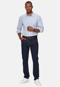 Camicia chiara azzurra con tasca, abbinata a jeans blu scuro e sneakers bianche. Vestibilità dritta. Design minimalista senza motivi.