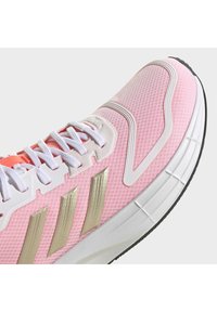 Scarpa da atletica rosa chiaro con tomaia in rete traspirante, strisce dorate, lacci bianchi e suola testurizzata con accenti neri.