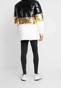 Pufuňák s černými, zlatými a bílými částmi, s lesklým povrchem. V kombinaci s černými legínami a bílými teniskami.