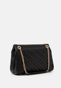 Mustikka tikkauksilla varustettu musta nahkalaukku, jossa on kultaketju ja vetoketjukiinnitys. Laukussa on tilava pääosio.