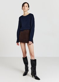 Maglione blu navy con vestibilità ampia, abbinato a una minigonna in velluto marrone. La modella indossa stivali di pelle neri alti fino al ginocchio con tacco.
