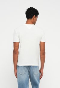 Balta trumpa rankovė t-shirt su V formos iškirpte, su tekstūruotu paviršiumi ir tiesiu apvadu, dėvima su šviesiai mėlynomis džinsomis.