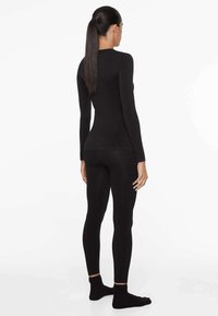 Schwarzes langärmliges Oberteil und Leggings aus dehnbarem Material. Das enganliegende Design folgt den Konturen des Körpers und hat keine sichtbaren Muster oder Akzente.