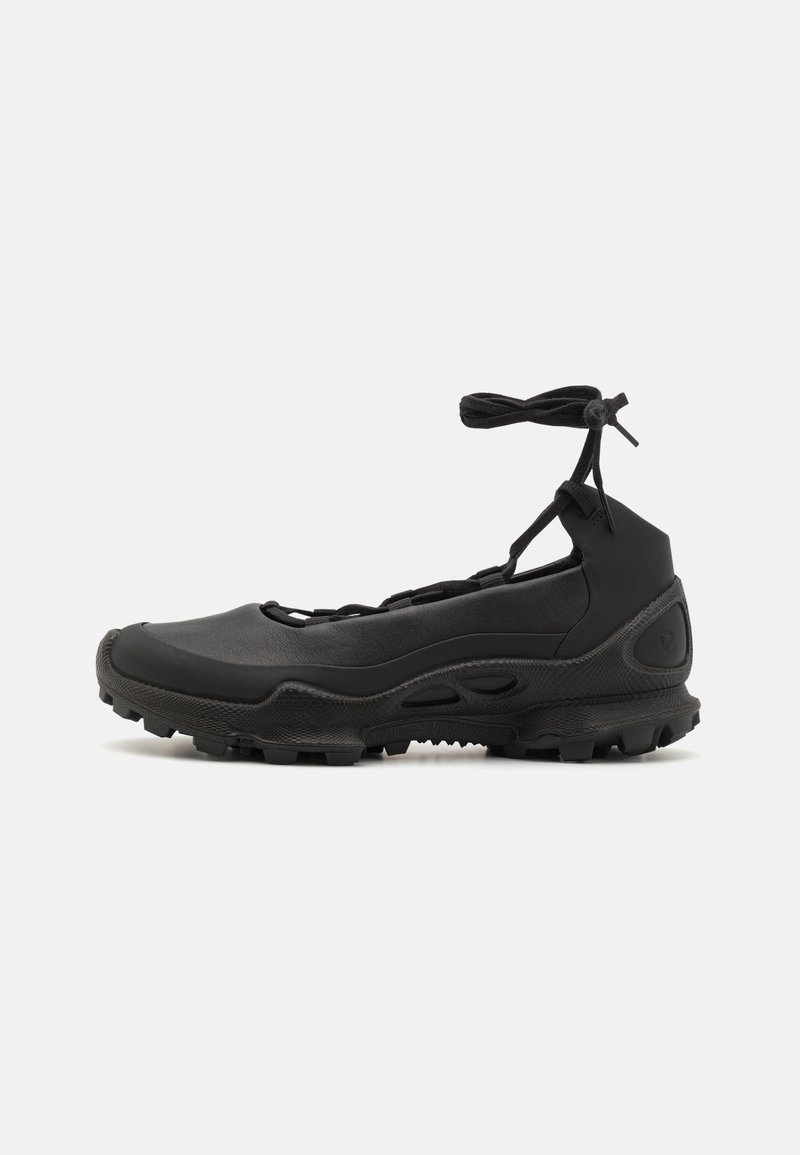 Chaussure de sport noire avec semelle robuste, détails découpés et lien à la cheville, vue de profil sur fond clair.
