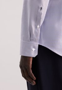 Camicia bianca e blu navy con un fine motivo geometrico, caratterizzata da colletto in contrasto e polsini con bottoni. Il tessuto sembra liscio.