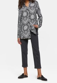 Svartvitt mönstrad långärmad blus med notchad krage, kombinerad med mörkgrå raka jeans och svarta slip-on skor.