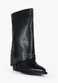 Stivale in pelle nera con gambale alto e morbido. Presenta dettagli con borchie argento lungo la caviglia e una punta appuntita. Tacco basso.