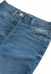 Vaqueros de mezclilla en azul medio con un diseño ajustado, que presentan un bolsillo frontal, cierre de botón metálico y detalles de desvanecimiento sutil.