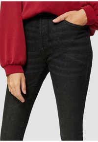Zwarte jeans van denim met een slim fit, voorzien van een hoge taille, subtiele textuur en een zijzak. Gecombineerd met een rood langemouwen top.