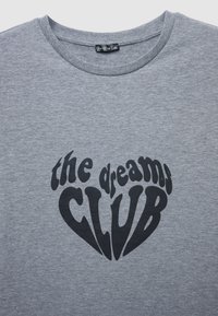 T-shirt en coton gris avec un grand texte noir indiquant "the dreams CLUB" dans une police ludique et audacieuse. Encolure arrondie, manches courtes.