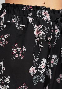 Gros plan sur un tissu noir avec un motif floral rose et blanc, et une taille élastique froncée avec un cordon de serrage noué en forme de nœud.