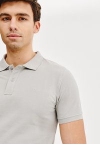 Jasnoszara koszulka polo wykonana z teksturowanej tkaniny, z klasycznym kołnierzykiem, dwoma guzikami i subtelnym logo na lewej piersi.