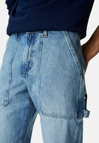 Pantalones de denim azul claro con un corte holgado, que presentan costuras visibles, bolsillos laterales y una textura suave. Con un bucle para cinturón como acento.