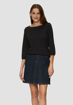 Zwarte blouse met lange mouwen, gecombineerd met een donkere spijkerrok in A-lijn met plooien en contrasterende stiksels, getoond op een neutrale achtergrond.