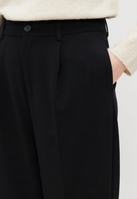 Pantaloni neri su misura con una texture liscia, dotati di chiusura a bottone singolo, tasche e un design a gamba dritta.