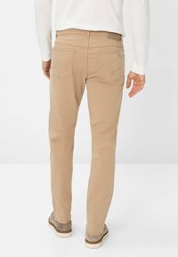 Beige Baumwollhosen mit geradem Bein, ausgestattet mit zwei Gesäßtaschen und dezenten Nähten. Getragen mit hellgrauen Schuhen.