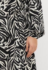Black and white patterned dress featuring a zebra-like design, long sleeves, and a tied waist detail, made from a smooth fabric.
