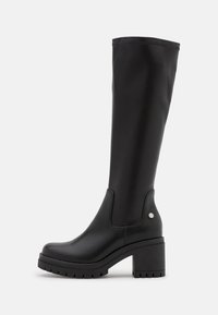 Bottes noires en cuir synthétique montant jusqu'aux genoux, avec une semelle à talon épais, des panneaux élastiques latéraux et un accent argenté circulaire sur le côté extérieur.