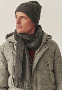 Grijze gebreide muts en bijpassende sjaal, beide met een geribbelde textuur. De jas is grijs met een opgeblazen ontwerp en een zak met ritssluiting.