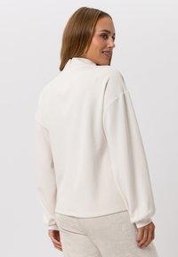 Roomkleurige sweatshirt met een hoge kraag, oversized pasvorm, geribbelde manchetten en een gladde textuur, gecombineerd met licht beige getextureerde broek.