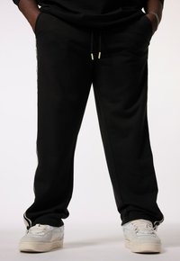 Schwarze Sweatpants mit lockerem Schnitt, ausgestattet mit Seitentaschen und einem Kordelzugbund. Kombiniert mit weißen Sportschuhen.