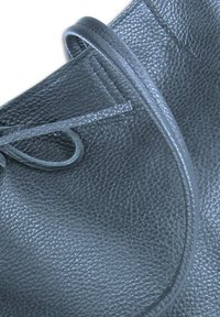 Zwarte lederen tas met een gestructureerd oppervlak, ronde vorm en een strikdetail. Gestikte randen versterken de duurzaamheid en het ontwerp.