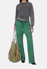 Gray cropped sweatshirt with text, green wide-leg trousers with side pockets, and a large green and gray bag. Smooth texture, casual fit.