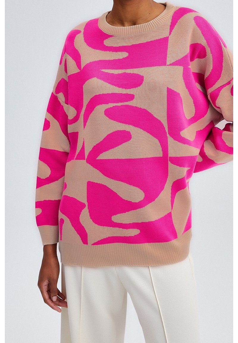 Gebreide trui in beige met gedurfde roze abstracte patronen. Heeft een ronde hals en een licht oversized pasvorm. Zachte textuur.