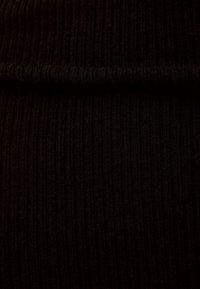 Tissu noir côtelé avec des lignes verticales ; texture douce ; léger ; présente un bord plié en haut pour une apparence sans coutures.