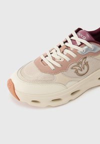 Baskets beige et rose clair avec une surface en mesh, des accents argentés et un logo en relief. Elles présentent une semelle crème avec des trous de ventilation.