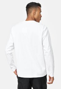 T-shirt bianco a maniche lunghe con collo rotondo, realizzato in morbido cotone, con un retro semplice. Presenta un'etichetta del marchio discreta vicino al collo.