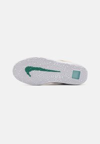 Biela podrážka tenisky s textúrovaným vzorom, s zeleným logom Nike. Hladké okraje a slabé vzory na povrchu pre lepšiu priľnavosť.