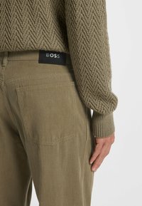 Pantaloni verde oliva con un maglione a maglia strutturata; le caratteristiche includono un'etichetta con logo, tasche posteriori e una forma aderente.