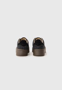 Zapatillas deportivas grises de fieltro con detalles en ante negro y suelas de goma marrón, que presentan un upper texturizado, un collar acolchado y acentos en contraste. Logotipo visible en el talón.