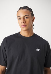 Black cotton t-shirt featuring a crew neck, short sleeves, and a small white New Balance logo on the left chest. Smooth texture.