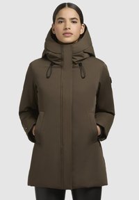 Brown, insulated parka with a high collar and hood. Features two front pockets and adjustable drawstrings. Smooth, matte fabric texture.