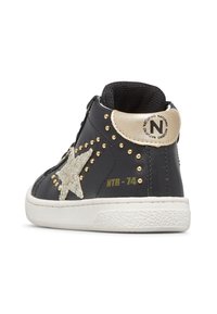 Sneaker alta nera con toppa a stella bianca, borchie dorate, linguetta beige con logo "N" e suola in gomma bianca.