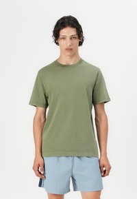 Oliven grøn bomulds-T-shirt med korte ærmer, rund hals og afslappet pasform. Båret med lyseblå shorts, minimalistisk design og uden synlige mønstre.